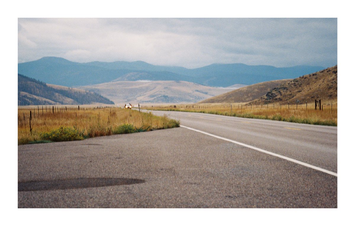A two-lane road winding through golden foothills toward blue mountains