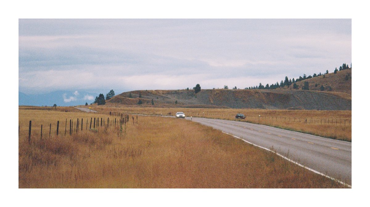 Two cars on a rural road crossing rolling grassland beneath low clouds