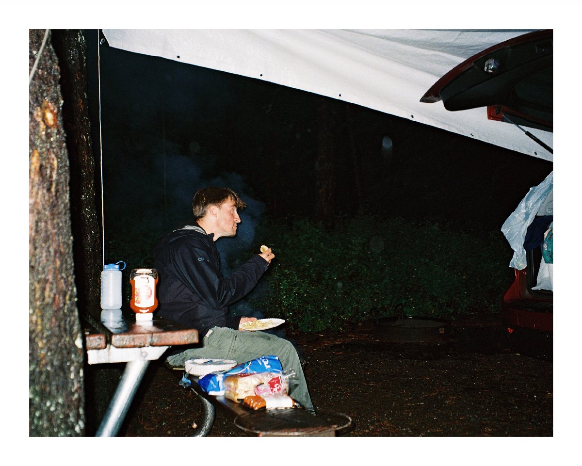 A camper eating at a picnic table beneath a tarp after dark
