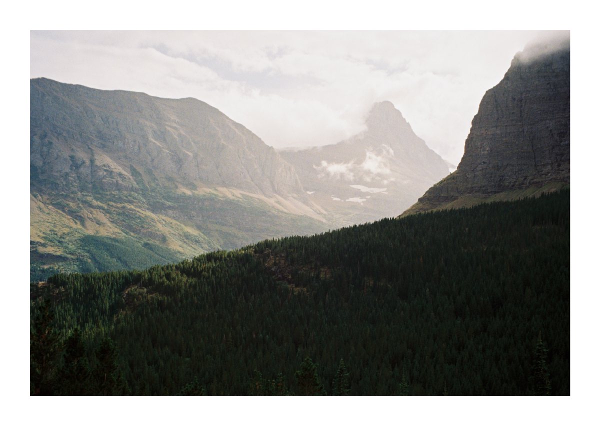 Clouds curling around a sharp mountain peak above a dark evergreen valley