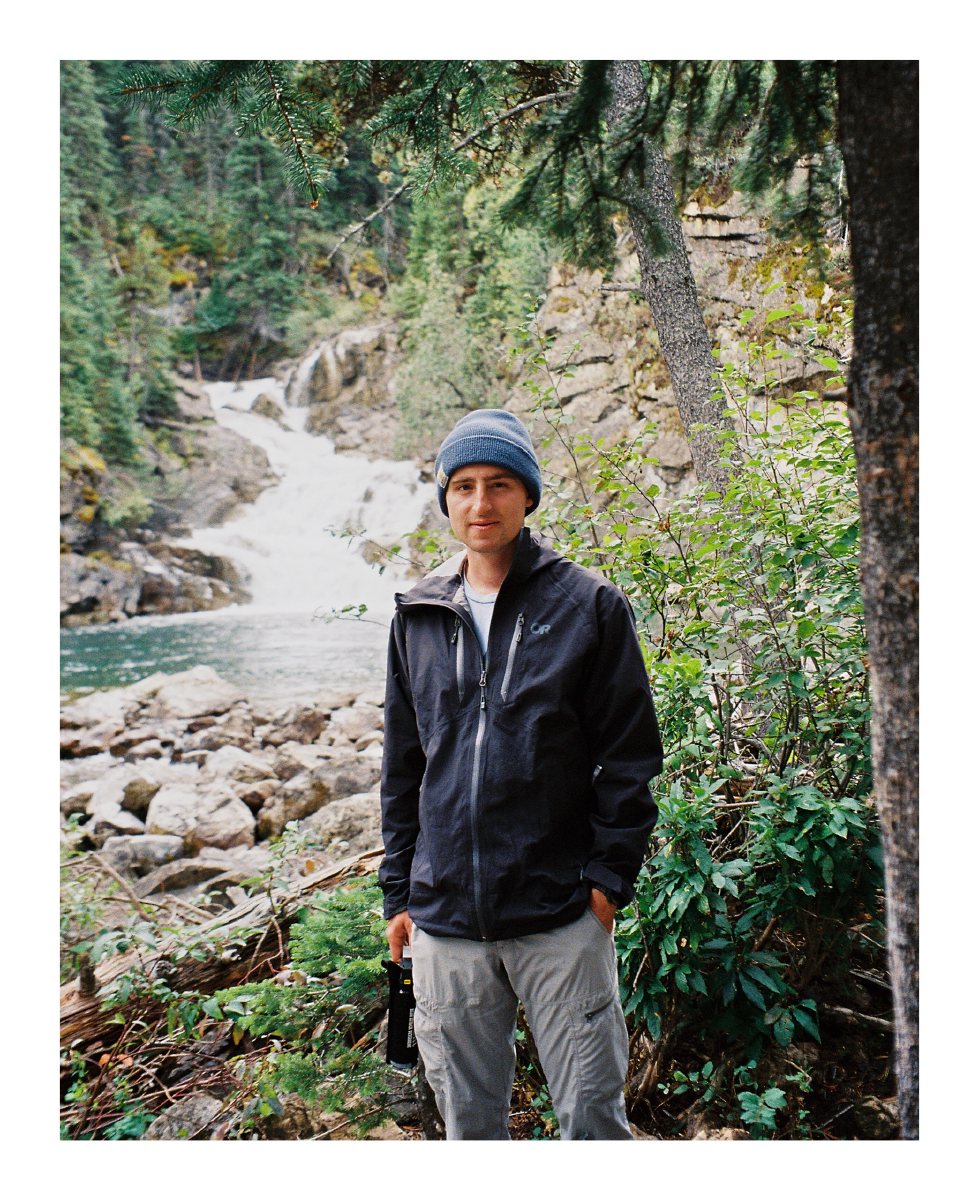 A backpacker in a blue beanie standing beside a forest waterfall
