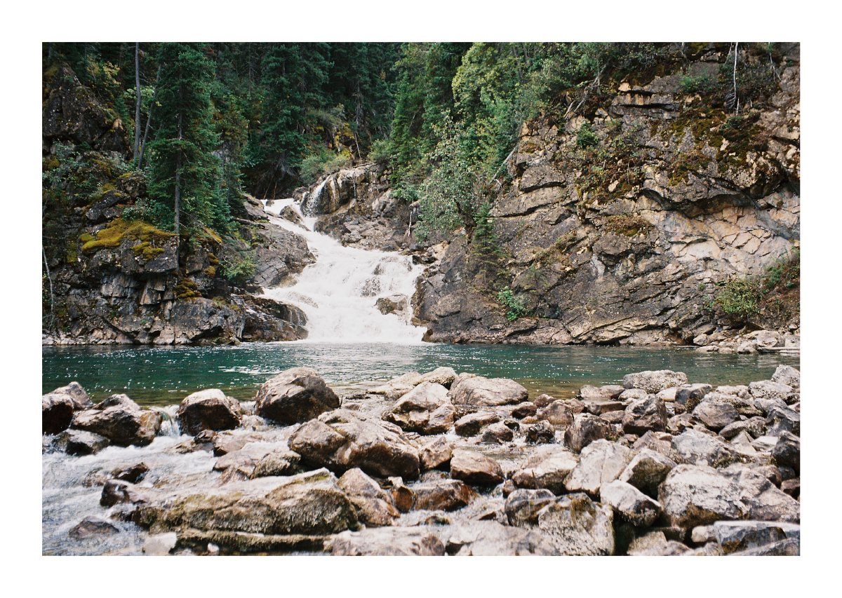 A waterfall cascading into a clear pool surrounded by boulders and forest