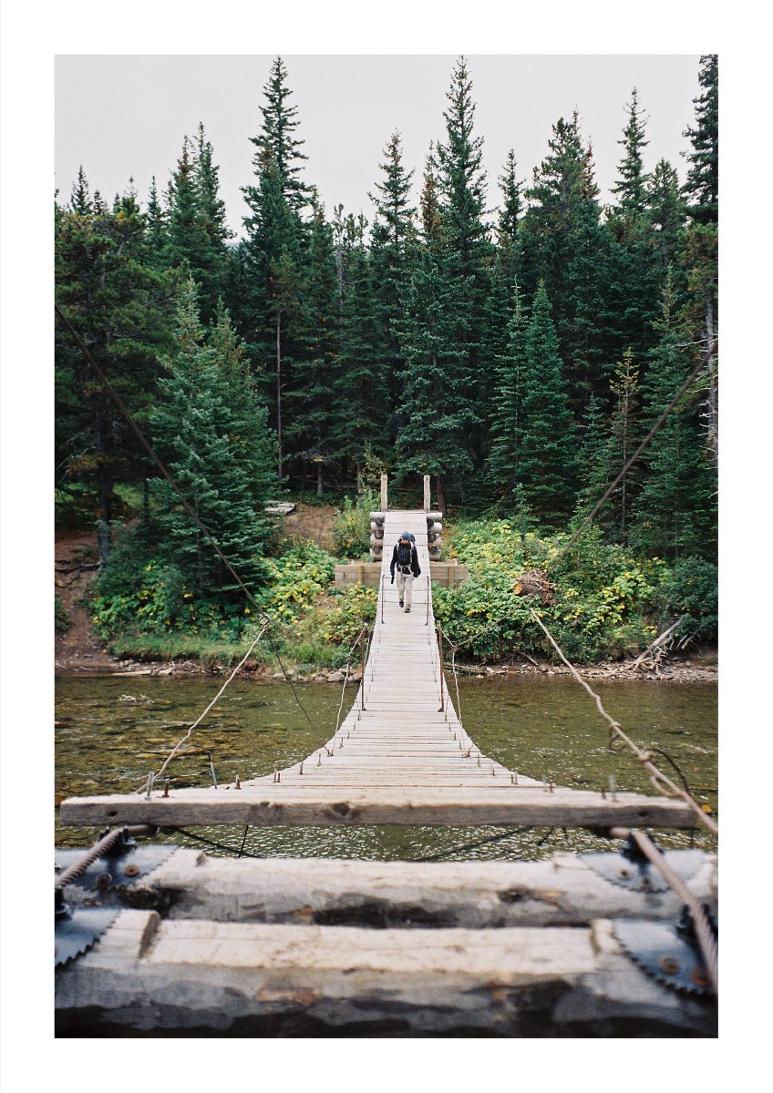 A backpacker crossing a narrow suspension bridge over a forest river