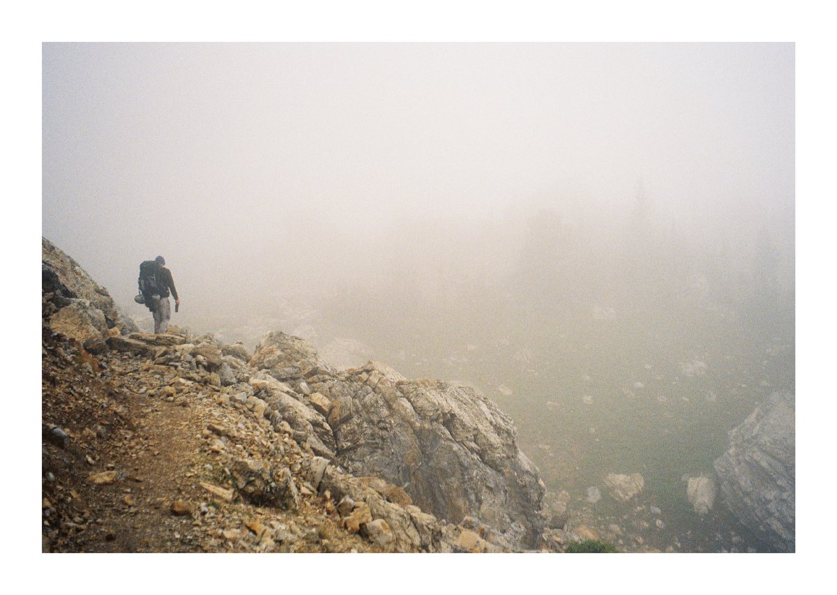 A lone backpacker descending a rocky trail into dense fog