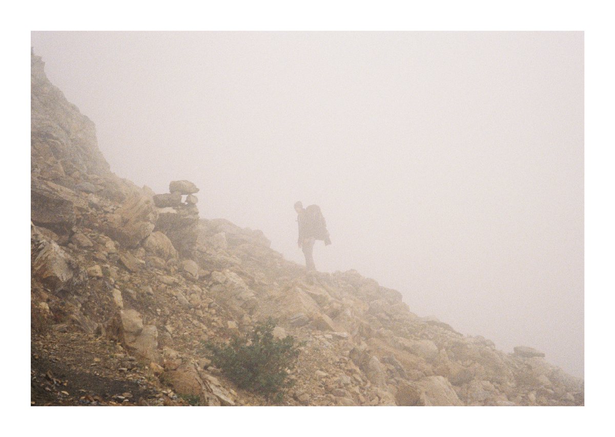 A backpacker passing a trail cairn on a fogbound rocky slope