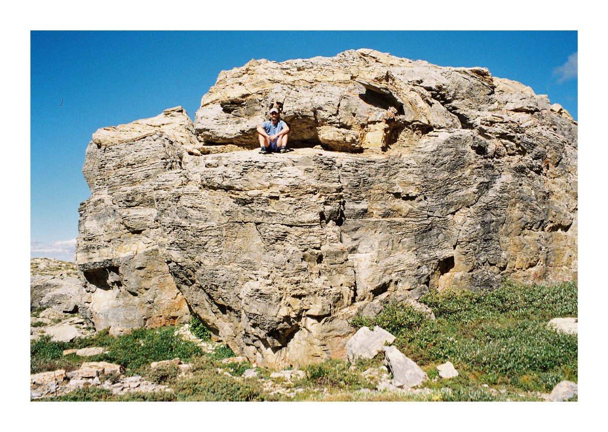A hiker seated in a broad ledge high on a sunlit rock formation