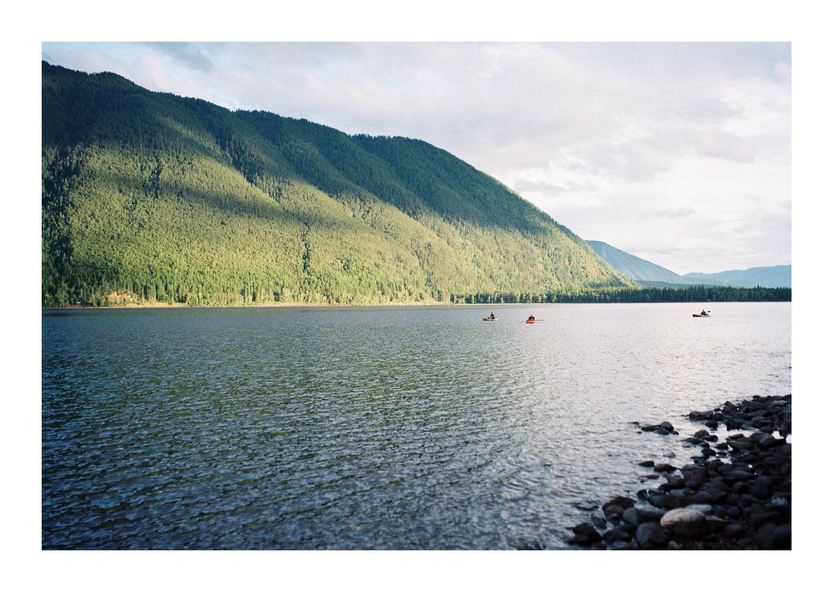 Three kayakers crossing a wide mountain lake in late-day light